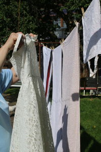 Cropped image of women holding dress while standing by clothesline in yard