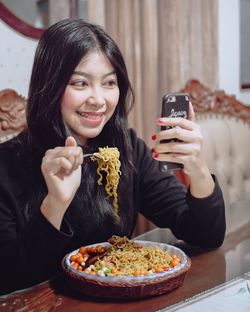 Portrait of smiling young woman using mobile phone while sitting on table