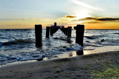 Wooden posts on beach against sky during sunset