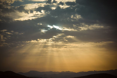 Low angle view of sunlight streaming through clouds during sunset