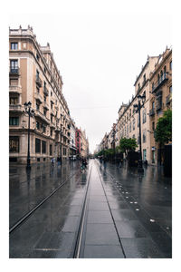 Wet street amidst buildings against sky in city