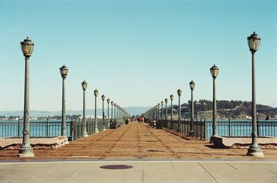 Walkway by sea against clear blue sky