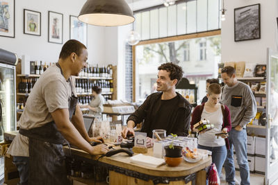 Male owner talking with customer at checkout counter in store