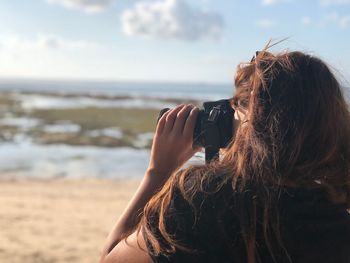 Side view of woman photographing sea against sky