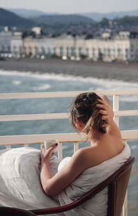 Woman having coffee while sitting against sea in city