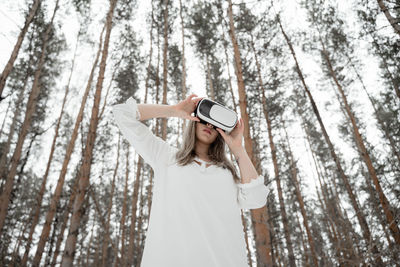 Low angel view of woman using vr against trees