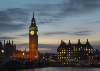 Illuminated clock tower in city against sky at night