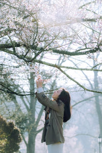 Rear view of young woman standing against bare tree