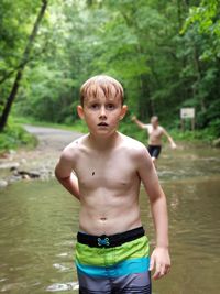 Portrait of shirtless boy standing against stream in forest