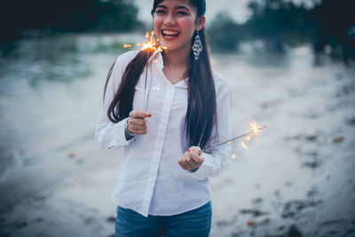 Portrait of teenage girl holding sparkler while standing outdoors