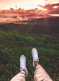 Low section of man standing on landscape against sky during sunset