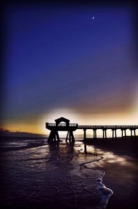 Silhouette lifeguard hut on beach against sky during sunset