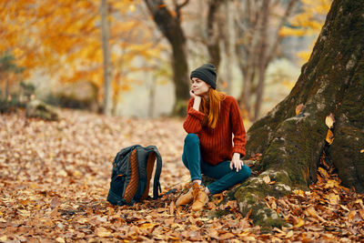 Full length of young woman sitting on tree during autumn