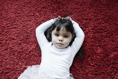 Portrait of cute baby girl lying on red carpet