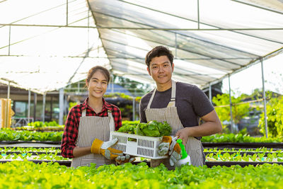 Full length of a smiling young woman standing in greenhouse