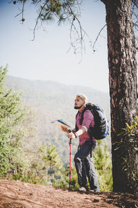 Man by tree trunk against sky