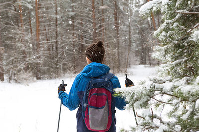 Skier with a backpack and hat with pompom with ski poles in his hands on background 