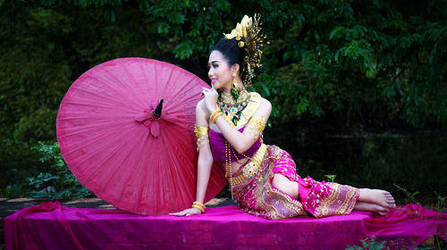 Young woman in traditional clothing with umbrella sitting at forest