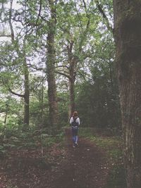 Full length of woman standing on tree trunk in forest