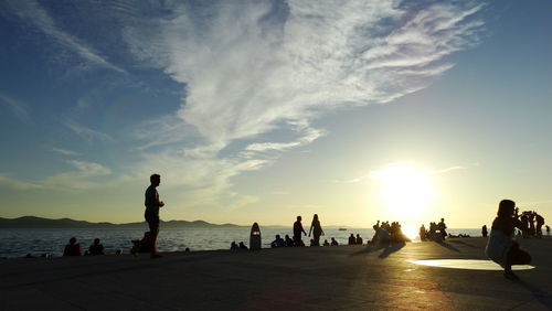 People on beach against sky during sunset