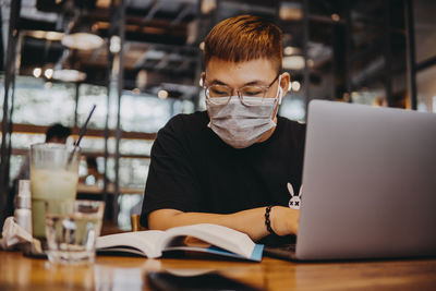 Young man wearing mask using laptop at cafe