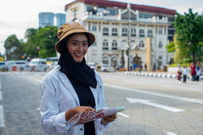 Portrait of smiling young woman standing on street in city