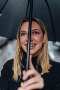 Close-up of thoughtful young woman holding umbrella during rain