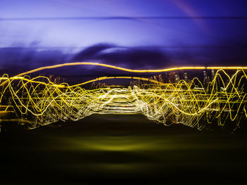 Light trails on landscape against sky at night