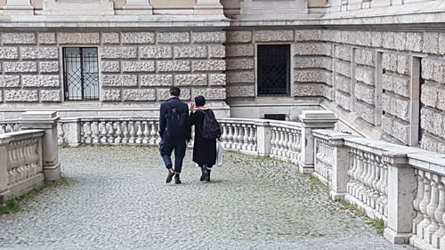 Rear view of man and woman walking on cobblestone street