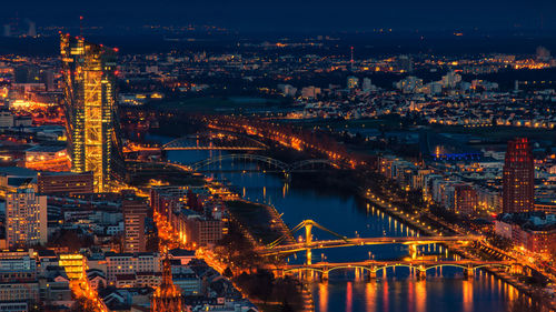 Illuminated bridge over river by buildings in city at night