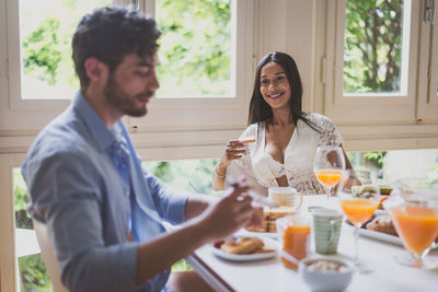 Smiling woman looking at boyfriend while having breakfast at home