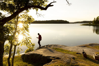 Side view of man standing on rock at lakeshore during sunset