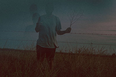 Rear view of man standing on land against sky during sunset