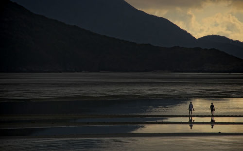 Silhouette people on beach against sky during sunset