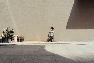 Girl standing on sidewalk against wall