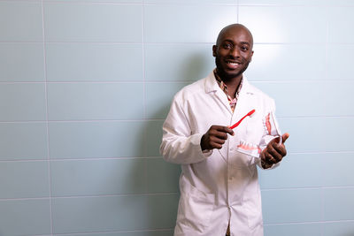 Portrait of dentist standing against wall