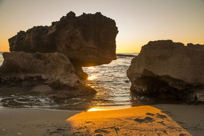 Rock formations on beach against sky during sunset