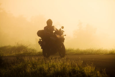 Man riding motorcycle on field against sky during sunset