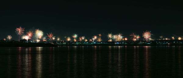 Illuminated city by river against sky at night