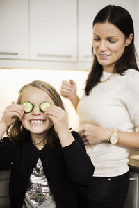 Mother looking at daughter covering eyes with cucumber slices