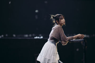 Side view of woman standing against black background