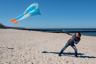 Man flying kite on beach against sky