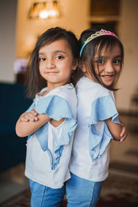 Portrait of smiling twin sisters standing back to back at home