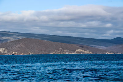 Scenic view of sea by mountain against sky