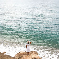 Rear view of woman standing on rock against sea