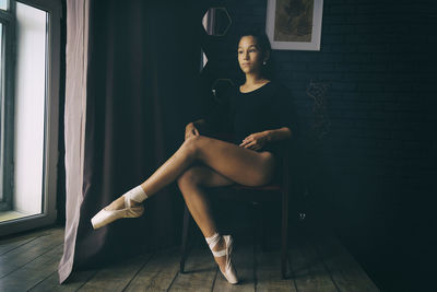 A young gentle and thoughtful ballerina poses in the interior and at the window