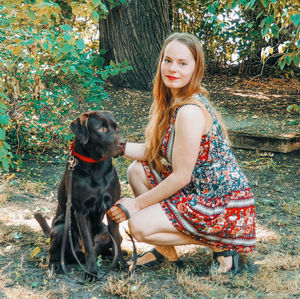 Young woman with dog sitting on plant against trees