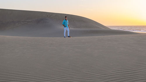 Rear view of woman walking on sand at beach against sky during sunset