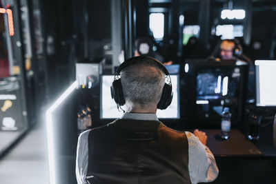 Rear view of senior man playing video game at gaming center during weekend