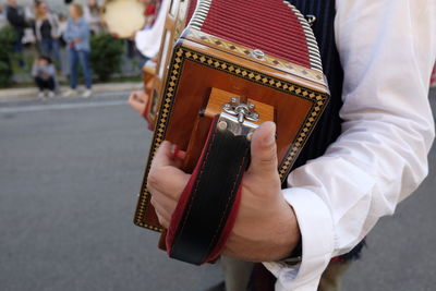 Midsection of man playing accordion while standing on road in city